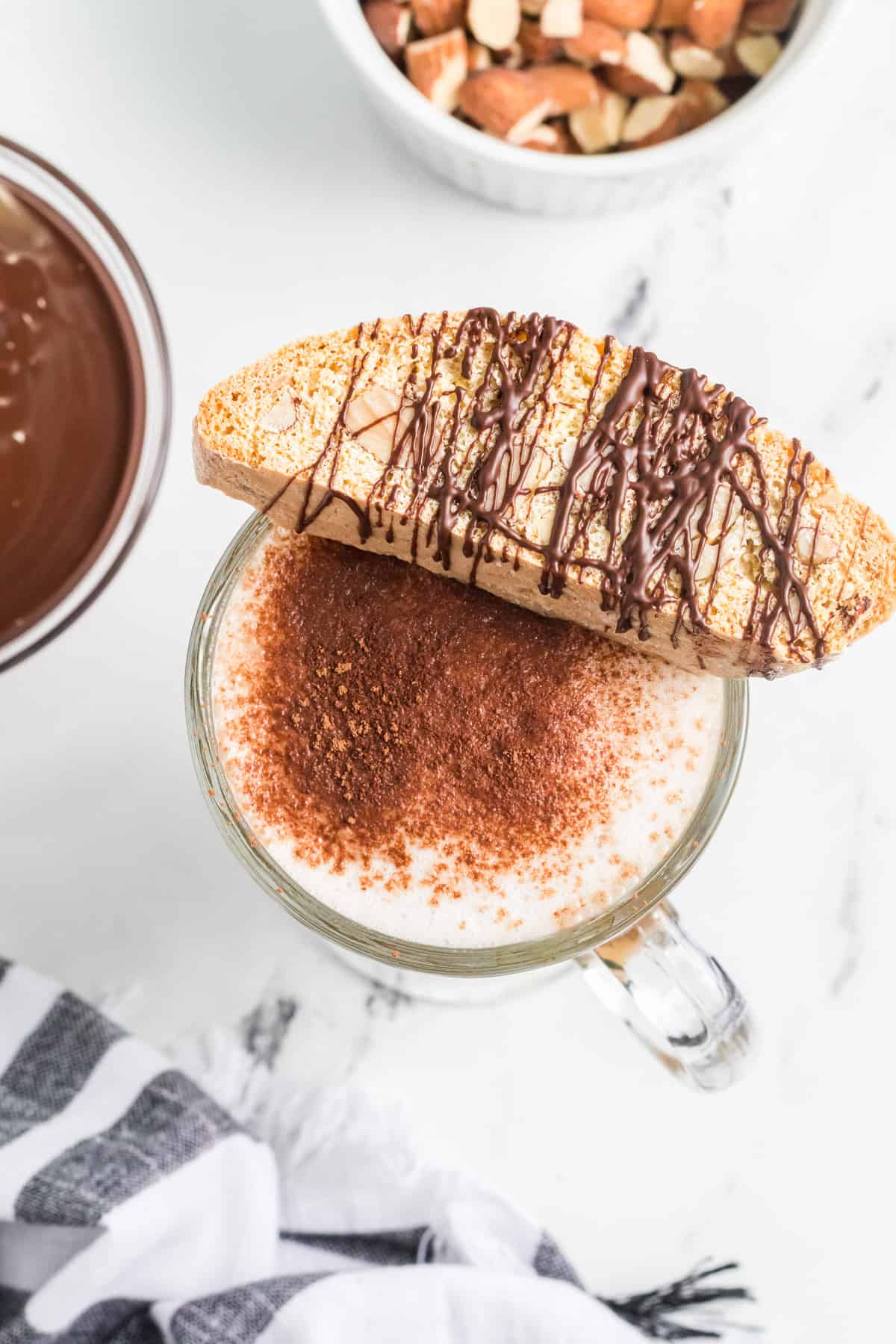 A chocolate covered almond biscotti resting on top of a cup of hot chocolate.