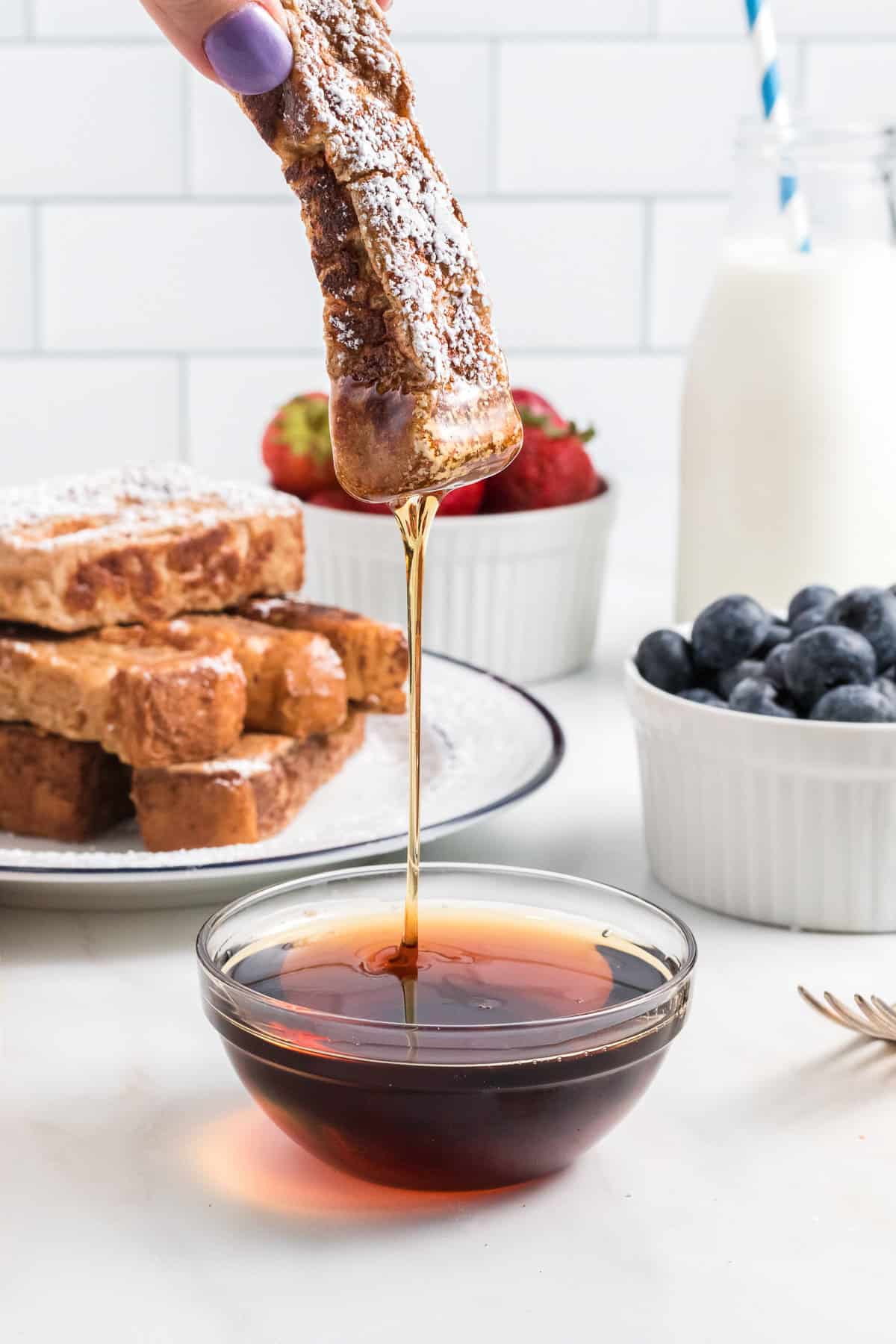 Dipping a French toast stick into a bowl of maple syrup.