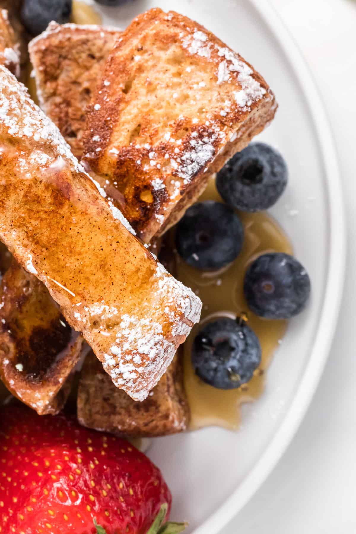 French toast sticks dusted with powdered sugar and drizzled with maple syrup.