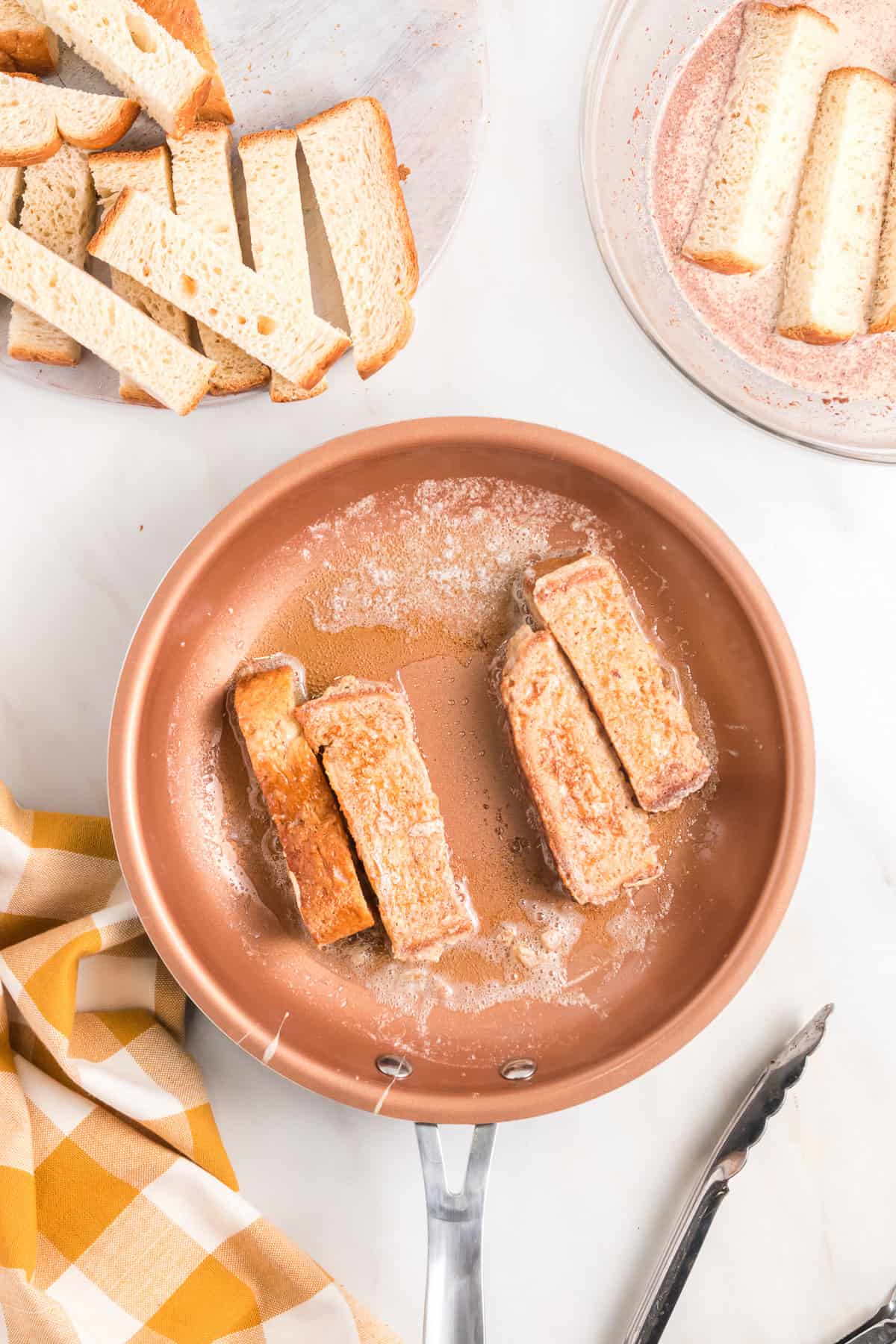 Frying French toast sticks in a pan with melted butter.