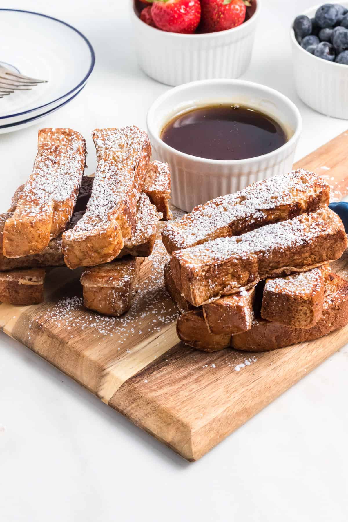 Stacks of French toast sticks dusted with powdered sugar on a wooden cutting board.