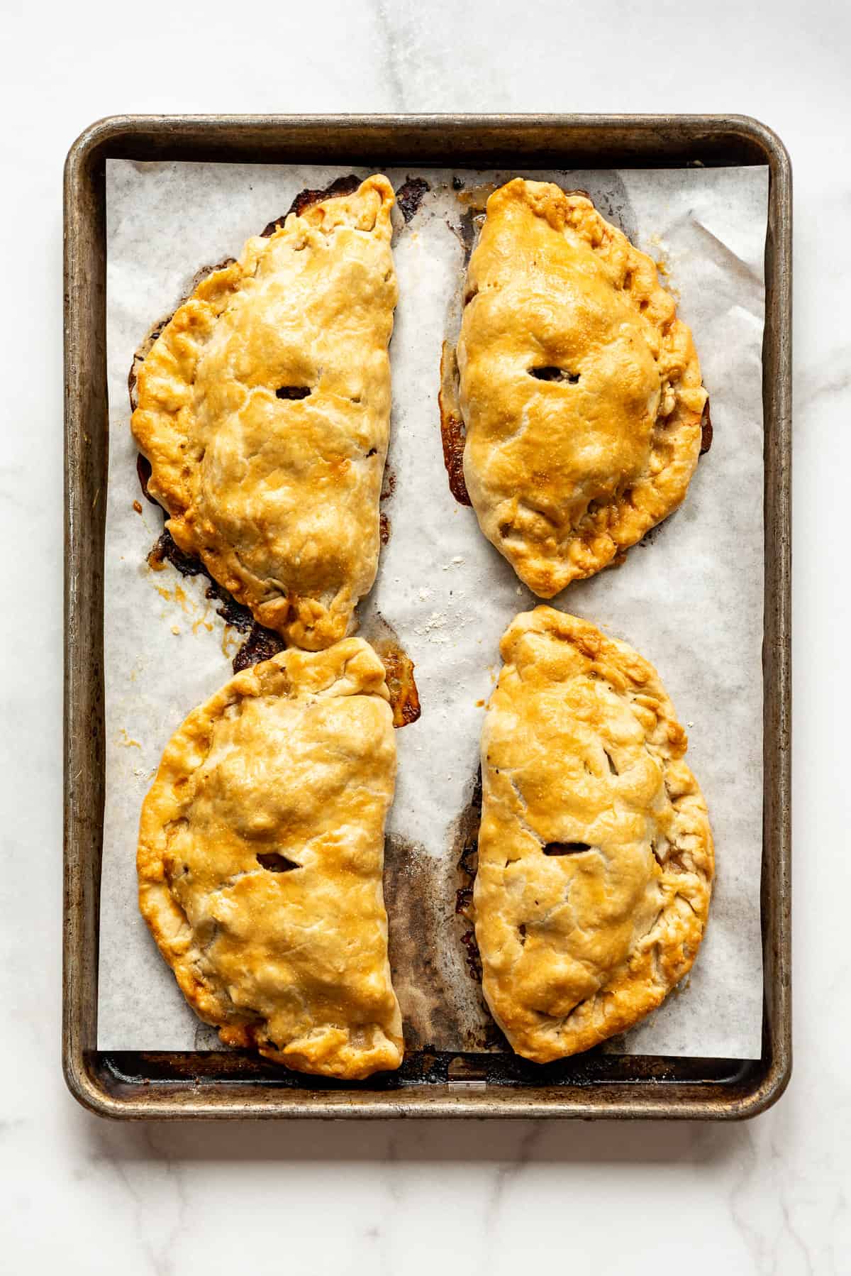 Four Cornish pasties on a baking sheet.