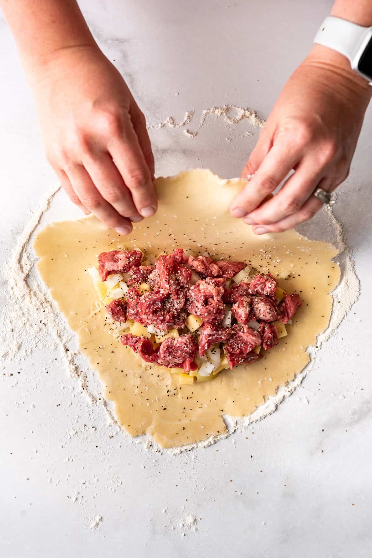 Folding pastry dough over a meat, potato, and rutabaga filling.