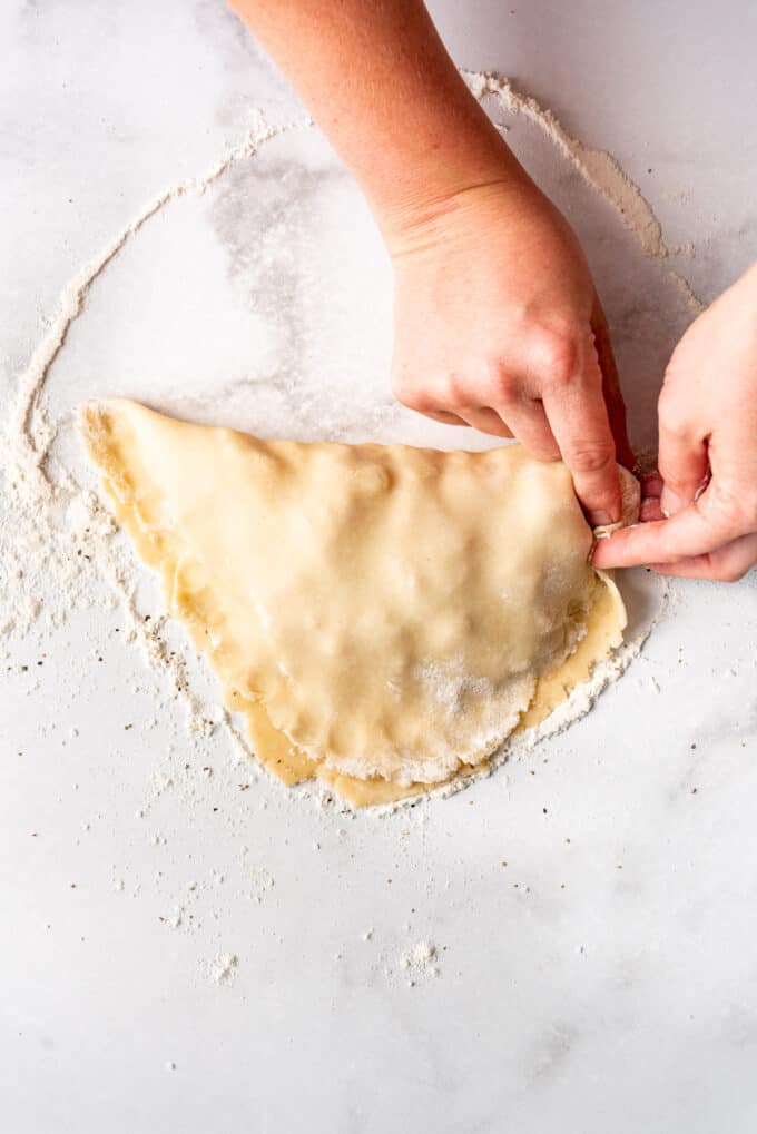 Using fingers to crimp the edges of a Cornish pasty closed to hold the filling inside while it bakes.