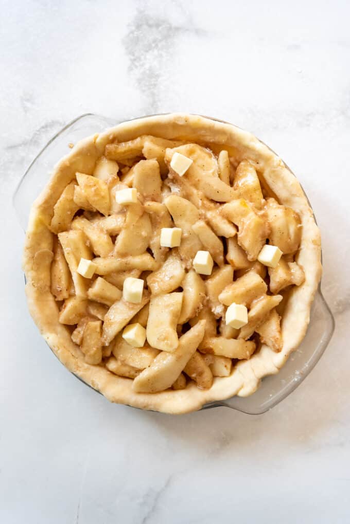 A pie crust in a glass pie plate filled with sliced pears tossed with flour, nutmeg, cinnamon, and sugar.