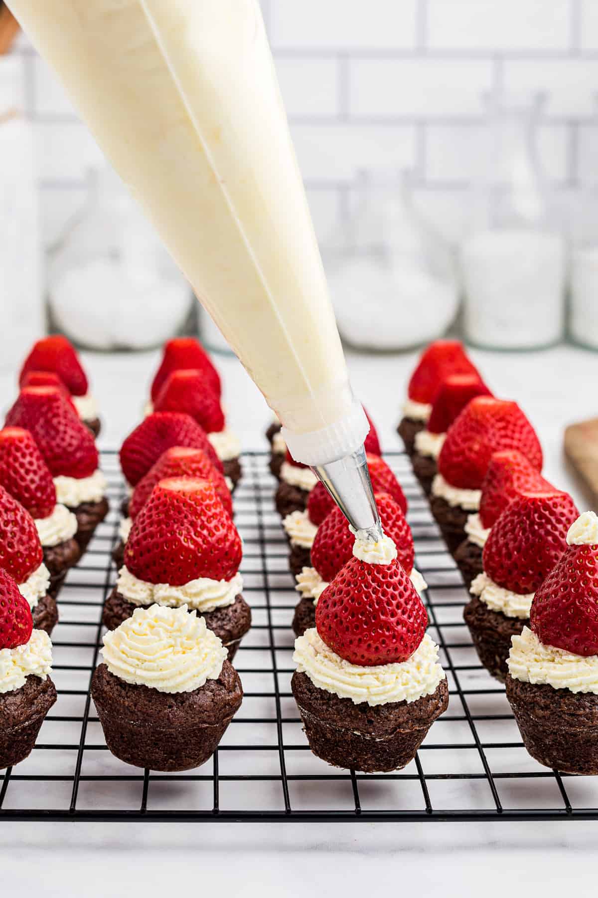 Adding a strawberry Santa hat and piping a dot of whipped cream on top of the brownie bites.