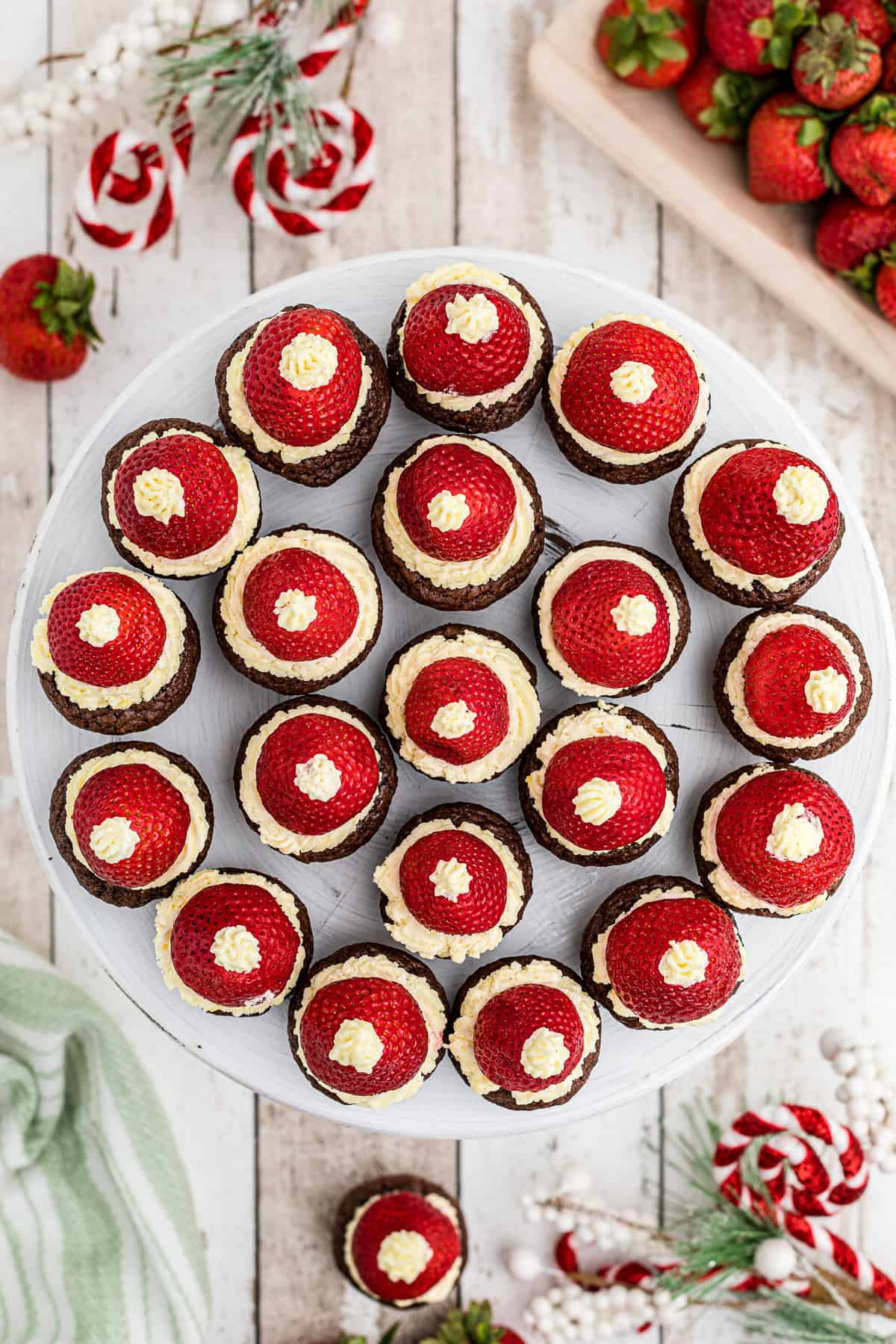 An overhead image of strawberry topped brownie bites on a white cake stand.