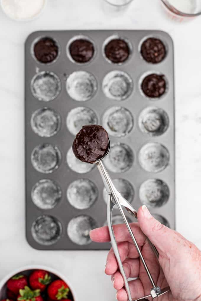 A small cookie scoop holding brownie batter over a mini muffin pan.