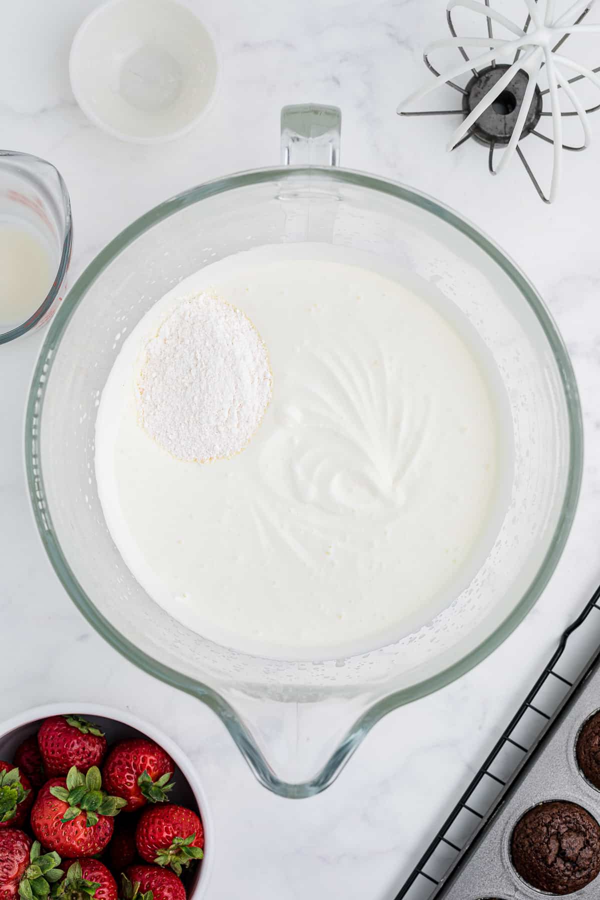 Adding instant vanilla pudding to whipped cream in a glass bowl.