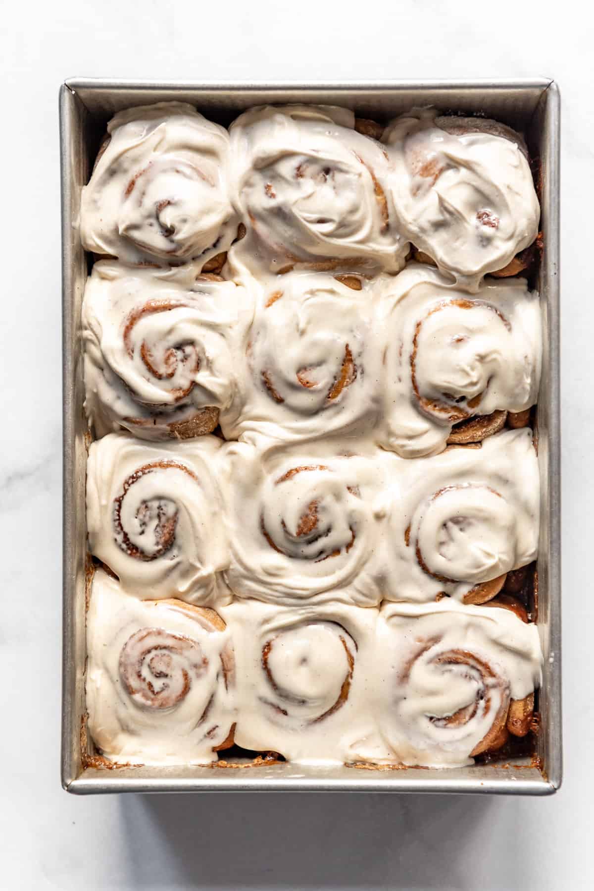 A pan full of homemade cinnamon rolls topped with cinnamon cream cheese frosting.