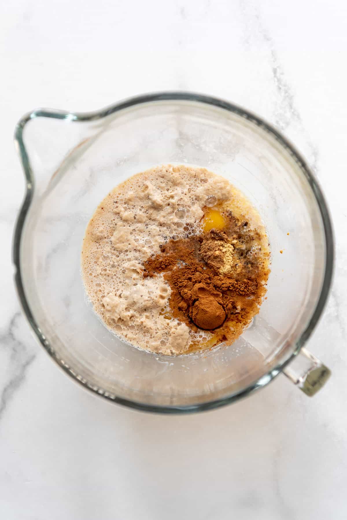 Adding yeast to butter, spices, and eggs in a large glass mixing bowl.