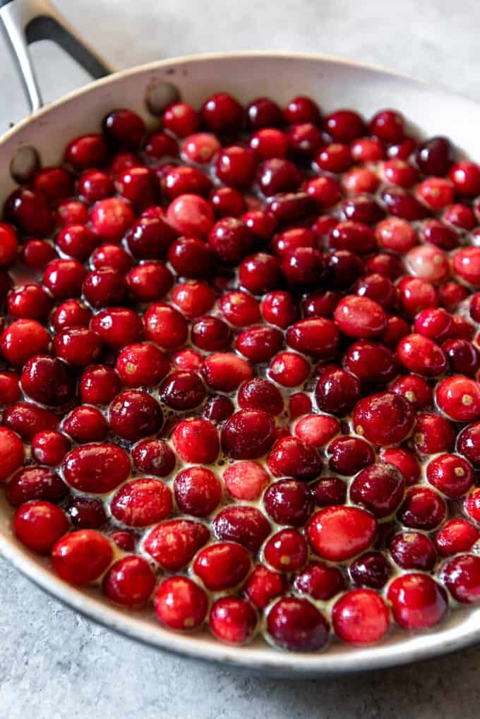 An image of a pan full of whole fresh cranberries in water, orange juice and sugar for making easy cranberry sauce for Thanksgiving.