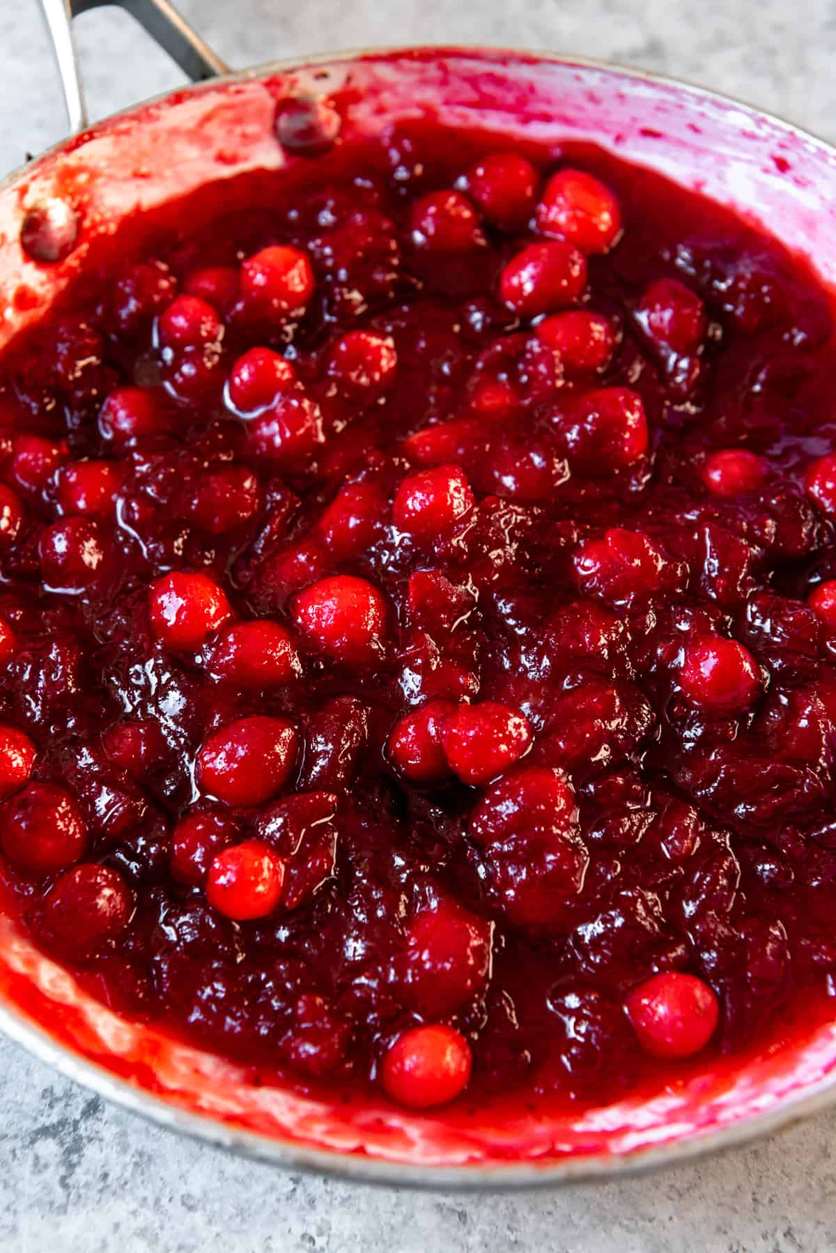 Top view of cranberries in a saucepan that have cooked down and burst into a jellied sauce.