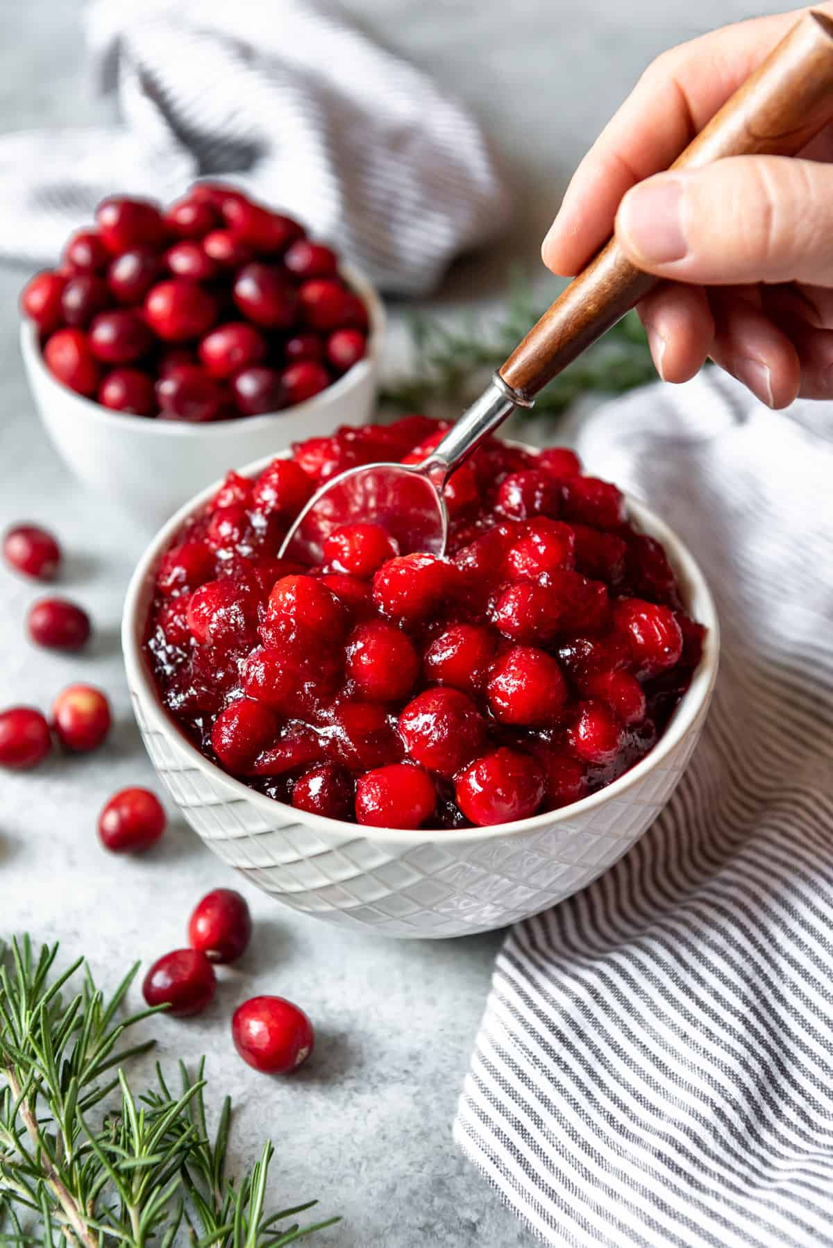 A hand holding a spoon in a bowl of homemade whole cranberry sauce.