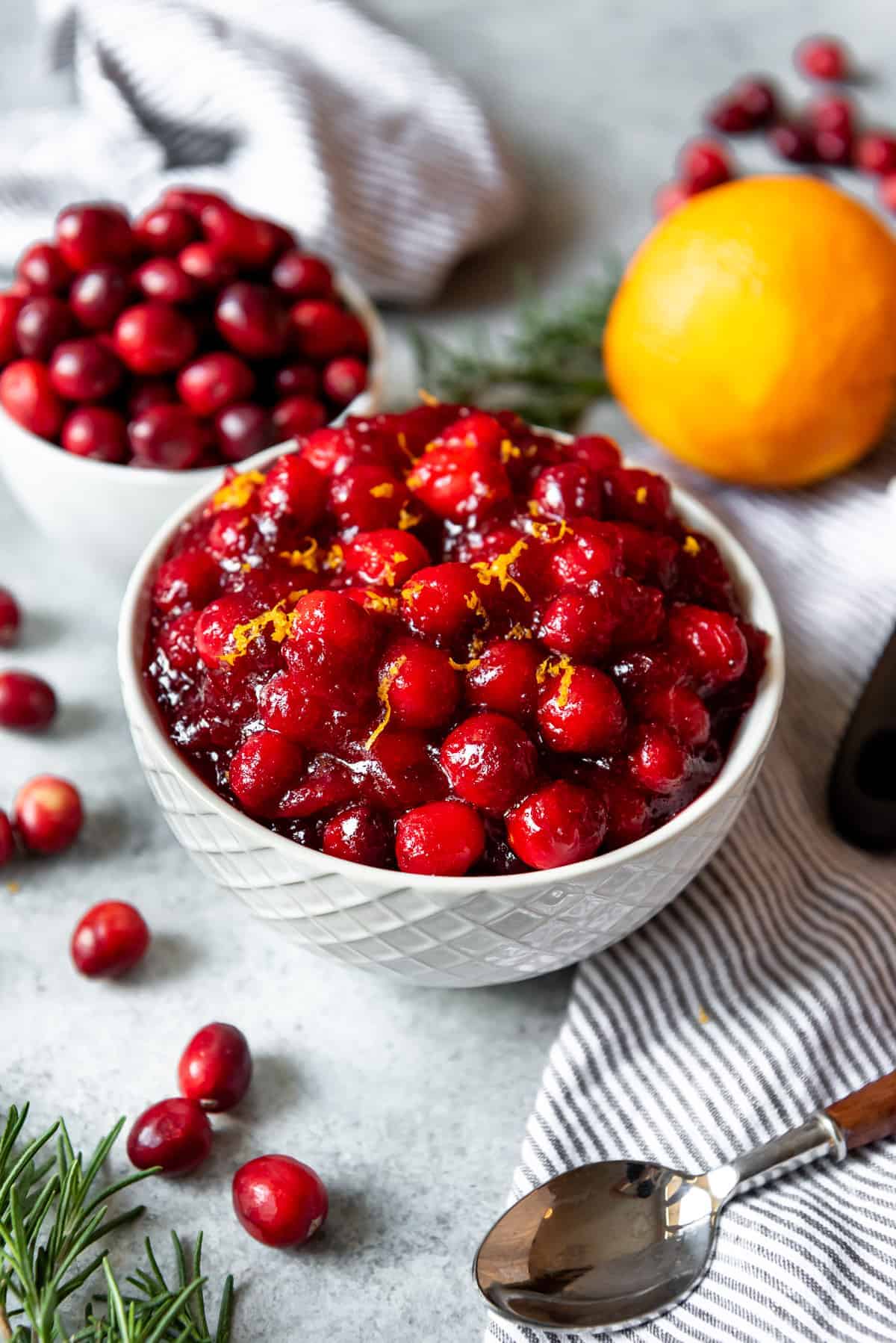 An image of a bowl of whole cranberry sauce with orange zest on top in a white serving bowl.