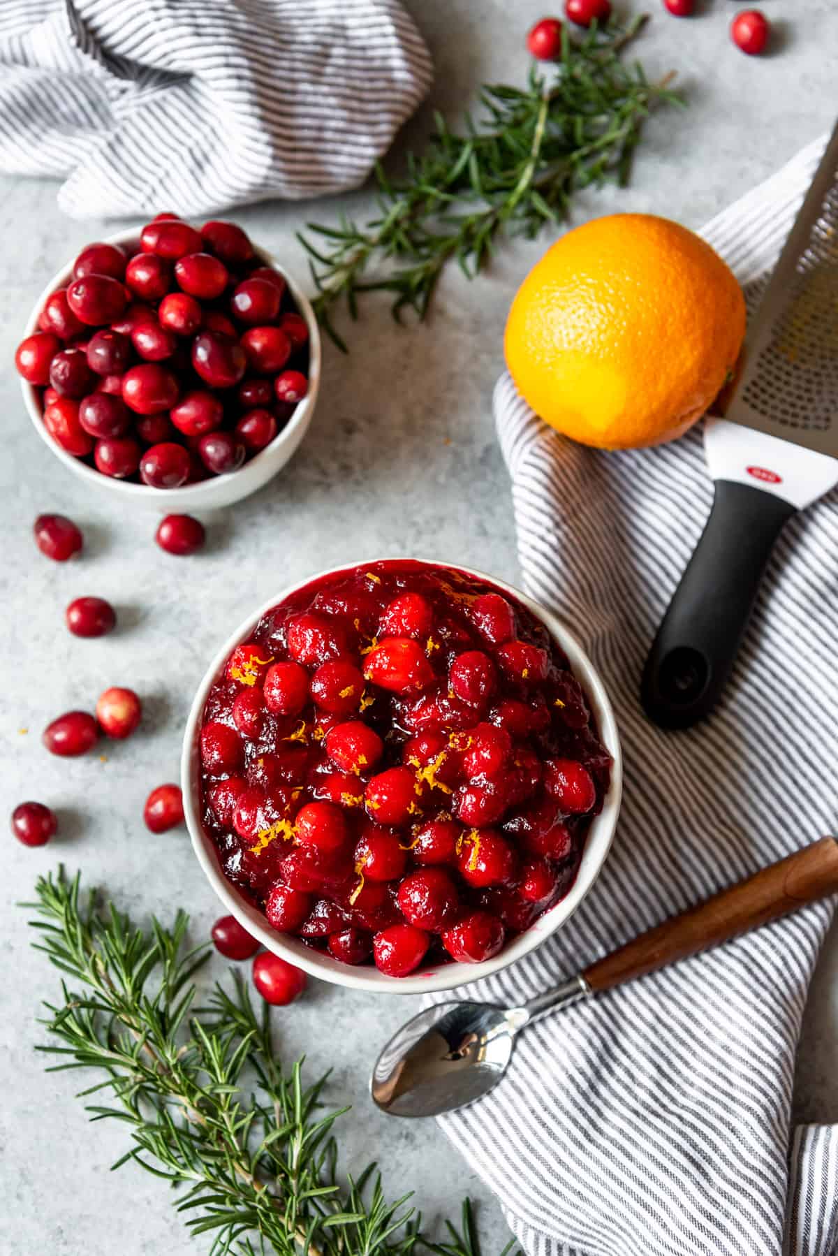 An image of a bowl of whole berry cranberry sauce in a white serving bowl, garnished with whole fresh cranberries and sprigs of rosemary.