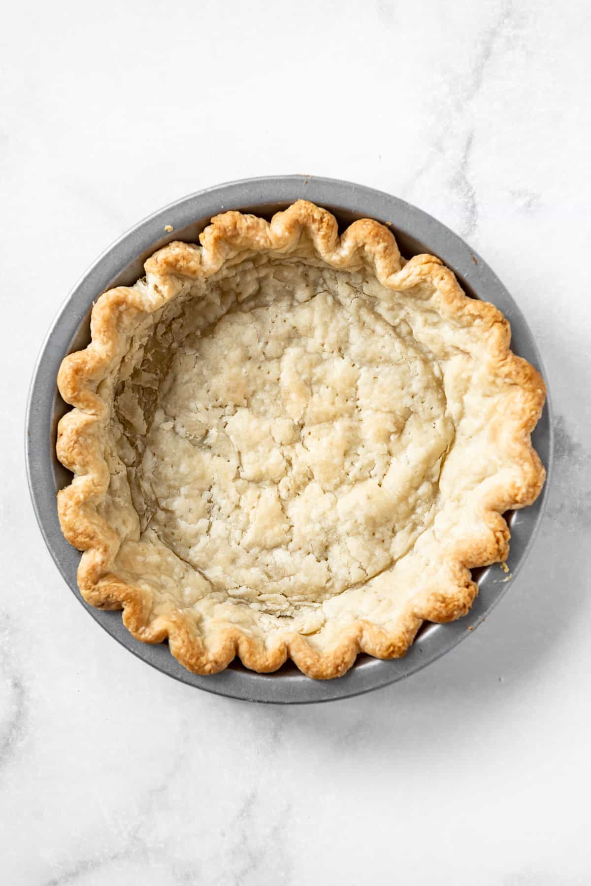 A full-baked homemade pie crust in a metal pie plate.
