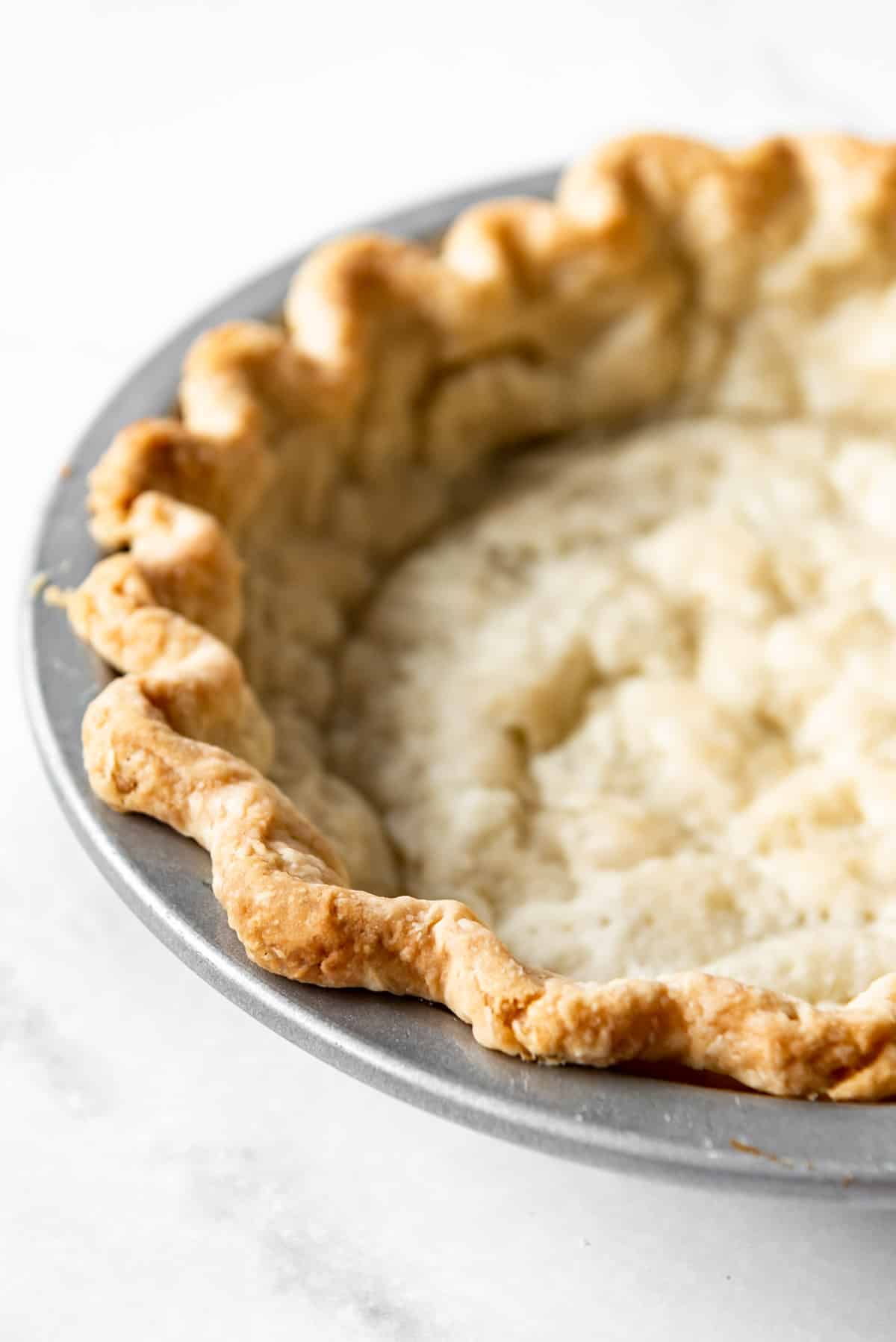 A full-baked pie crust in a metal pie plate.