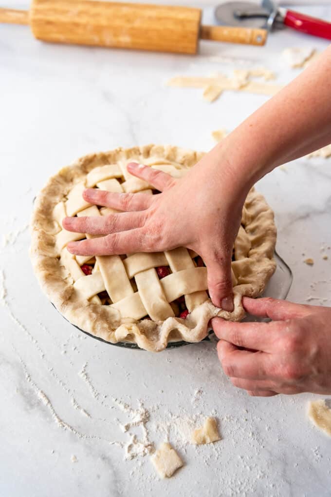 Crimping the edges of a homemade lattice pie crust using thumb and forefingers.