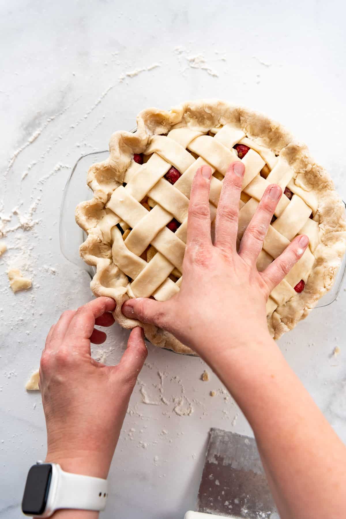 Thumb and forefinger being used to create a decorative crimped edge on a homemade pie crust with lattice design.