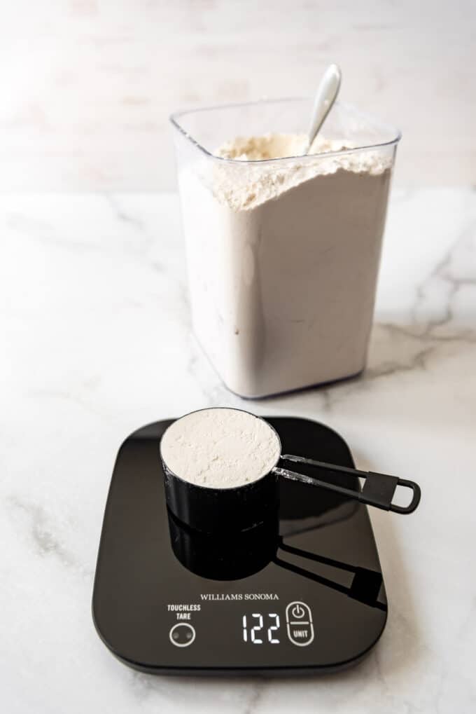 A cup of flour on a kitchen scale weighing 122 grams.