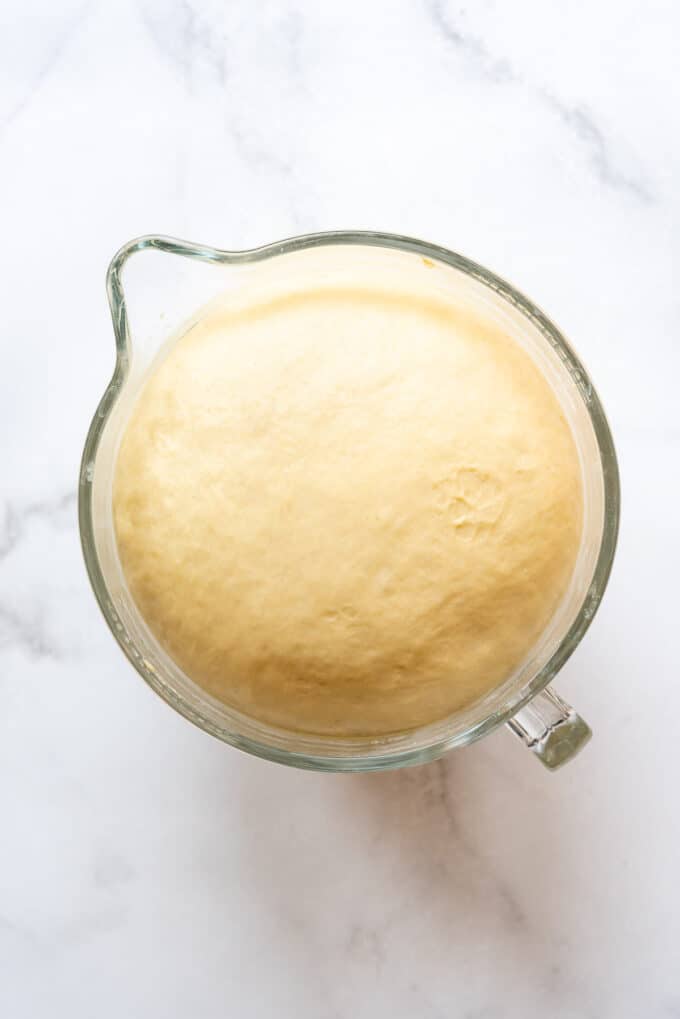 Risen yeast dough in a glass bowl that has increased by double in volume.