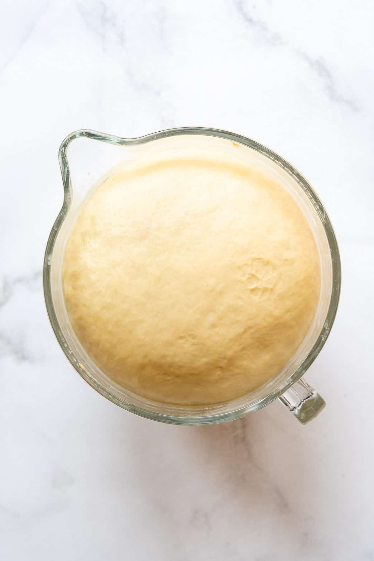 Risen yeast dough in a glass bowl that has increased by double in volume.