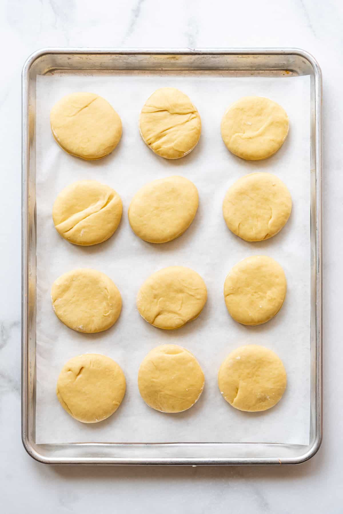 Twelve cut out donut dough circles on a baking sheet.