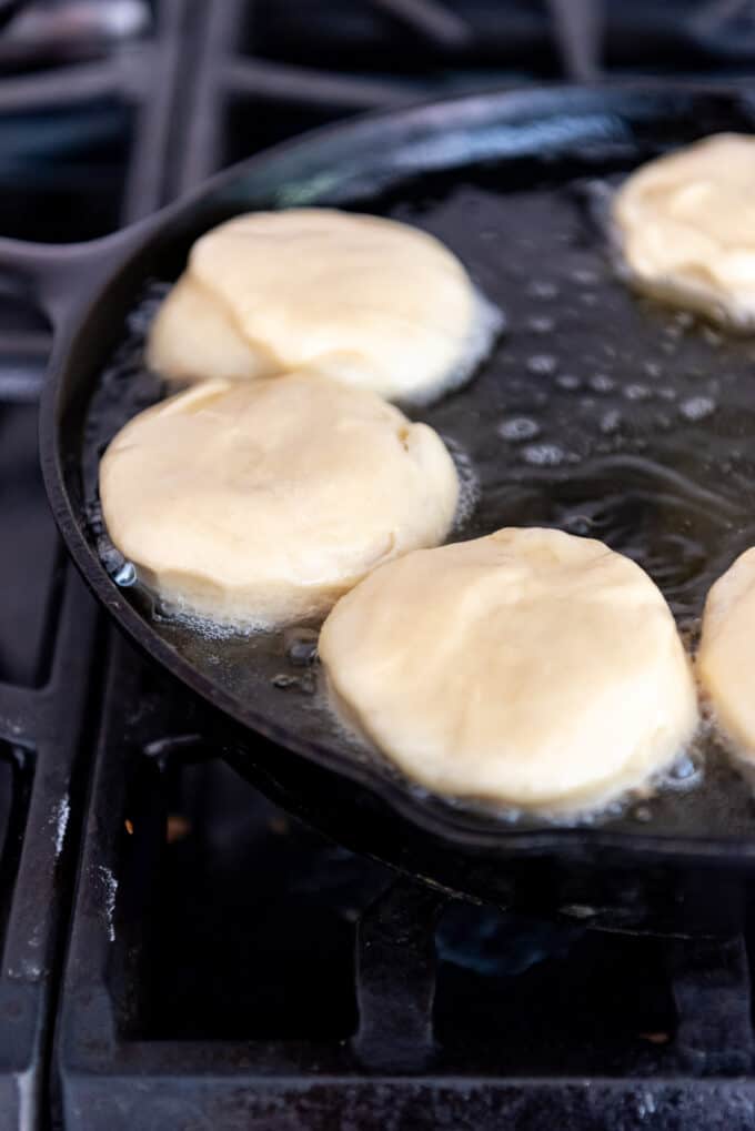 Round circles of yeast dough in hot oil in a pan.
