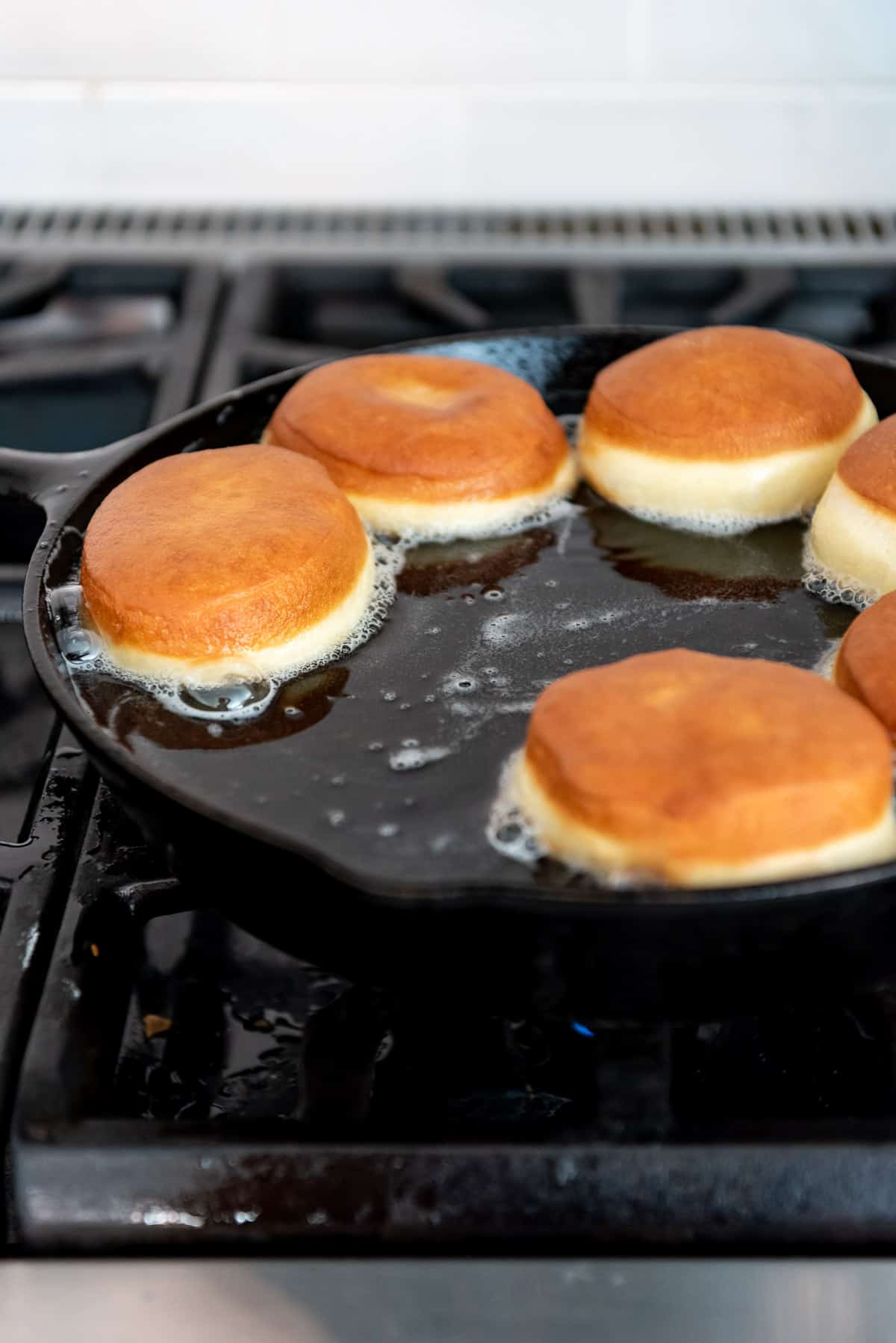 Golden brown donuts frying in oil in a pan on the stove.