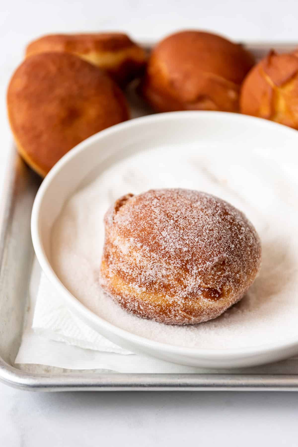 Rolling a homemade packzi donut in granulated sugar.