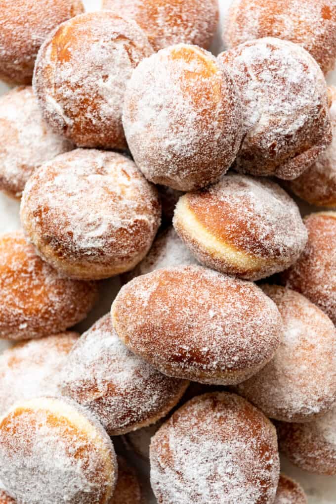 An image of piles of freshly fried donuts that have been tossed in granulated sugar.