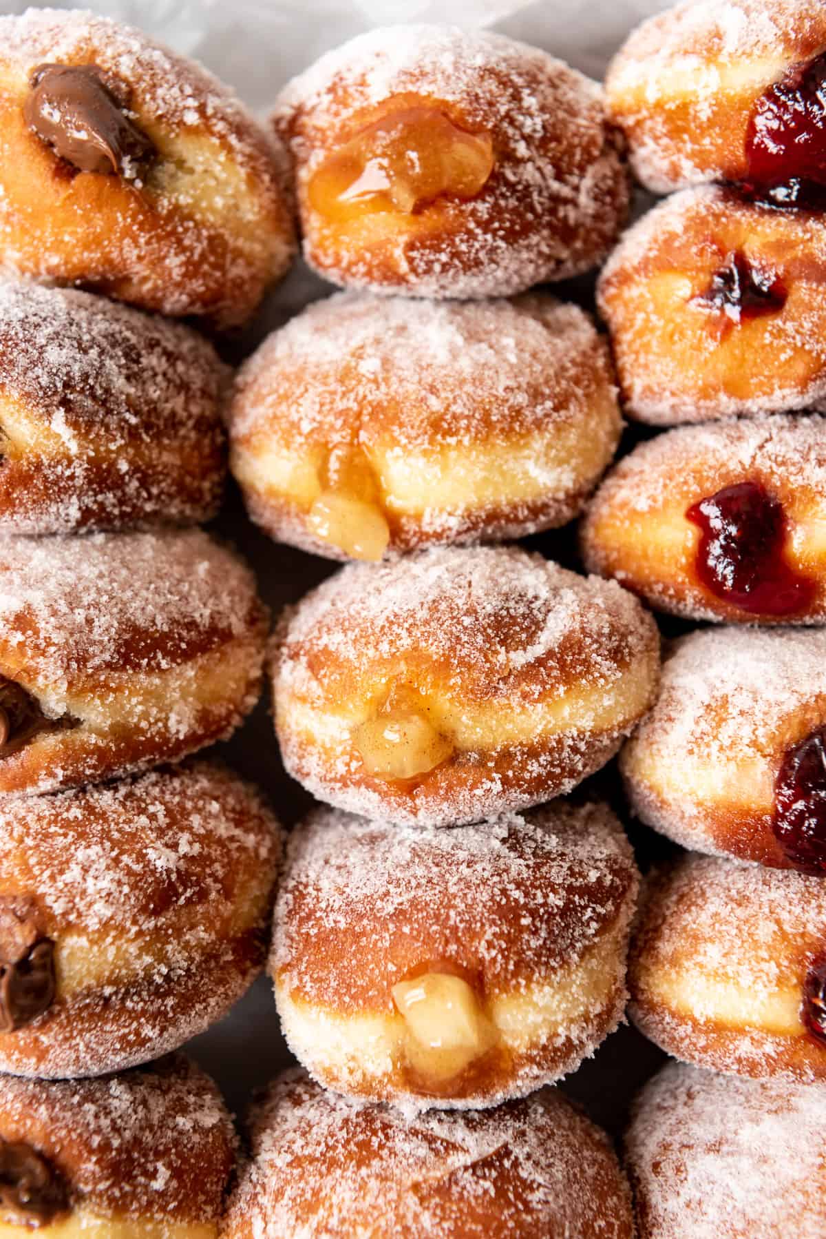 Apple, raspberry, and nutella filled jelly donuts with a white strip around the middle of each.