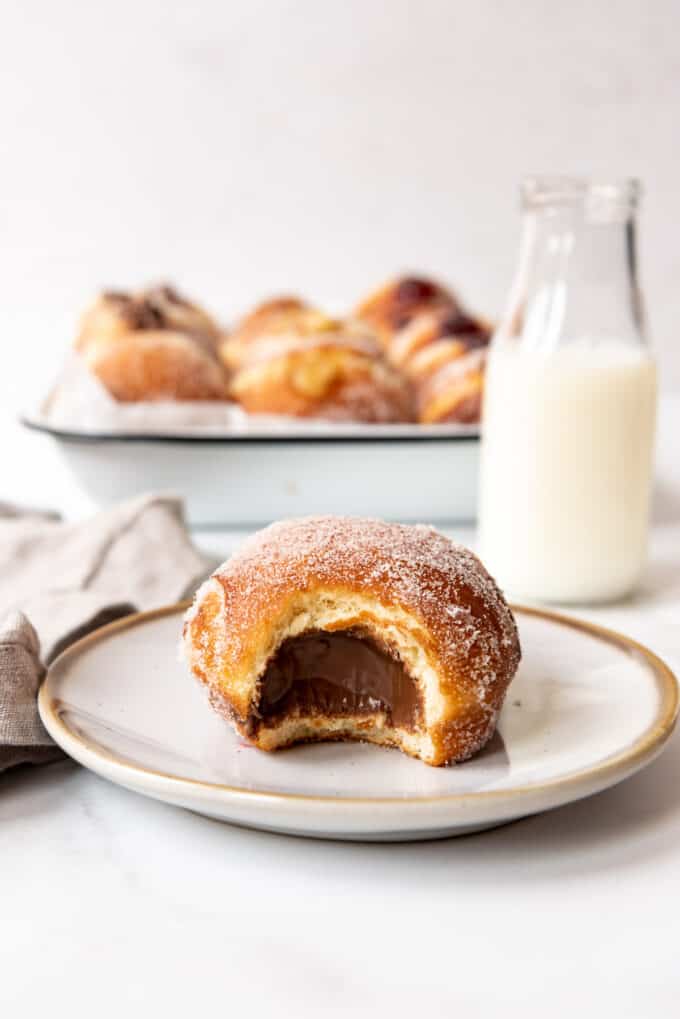 A packzi donut stuffed with nutella in front of a glass bottle of milk.
