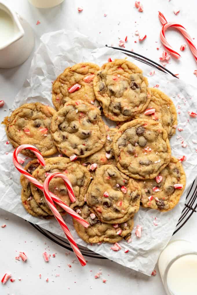 Peppermint chocolate chip cookies stacked on parchment paper with broken candy cane pieces around them.