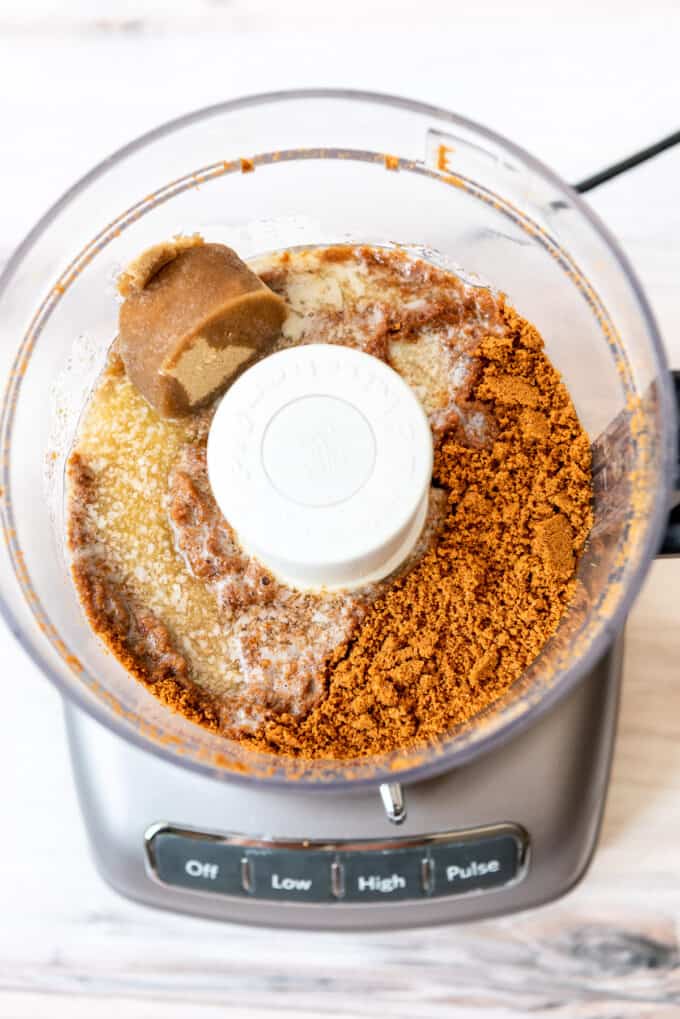 Adding melted butter and brown sugar to biscoff crumbs in a food processor.