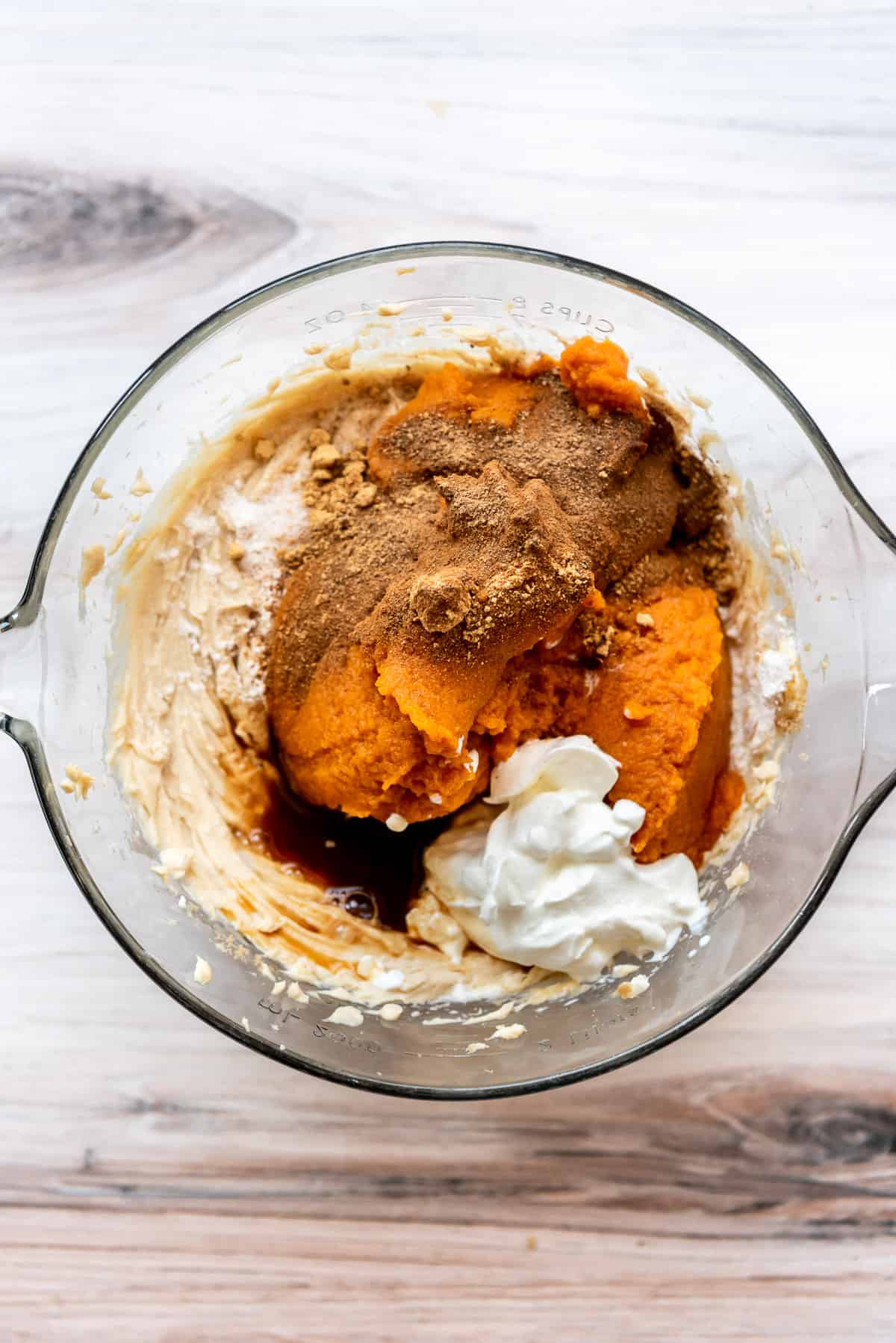 Adding pumpkin, sour cream, and spices to make pumpkin cheesecake filling.