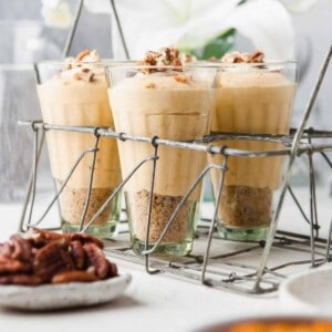 Three individual glass cups filled with no-bake pumpkin cheesecake mousse.
