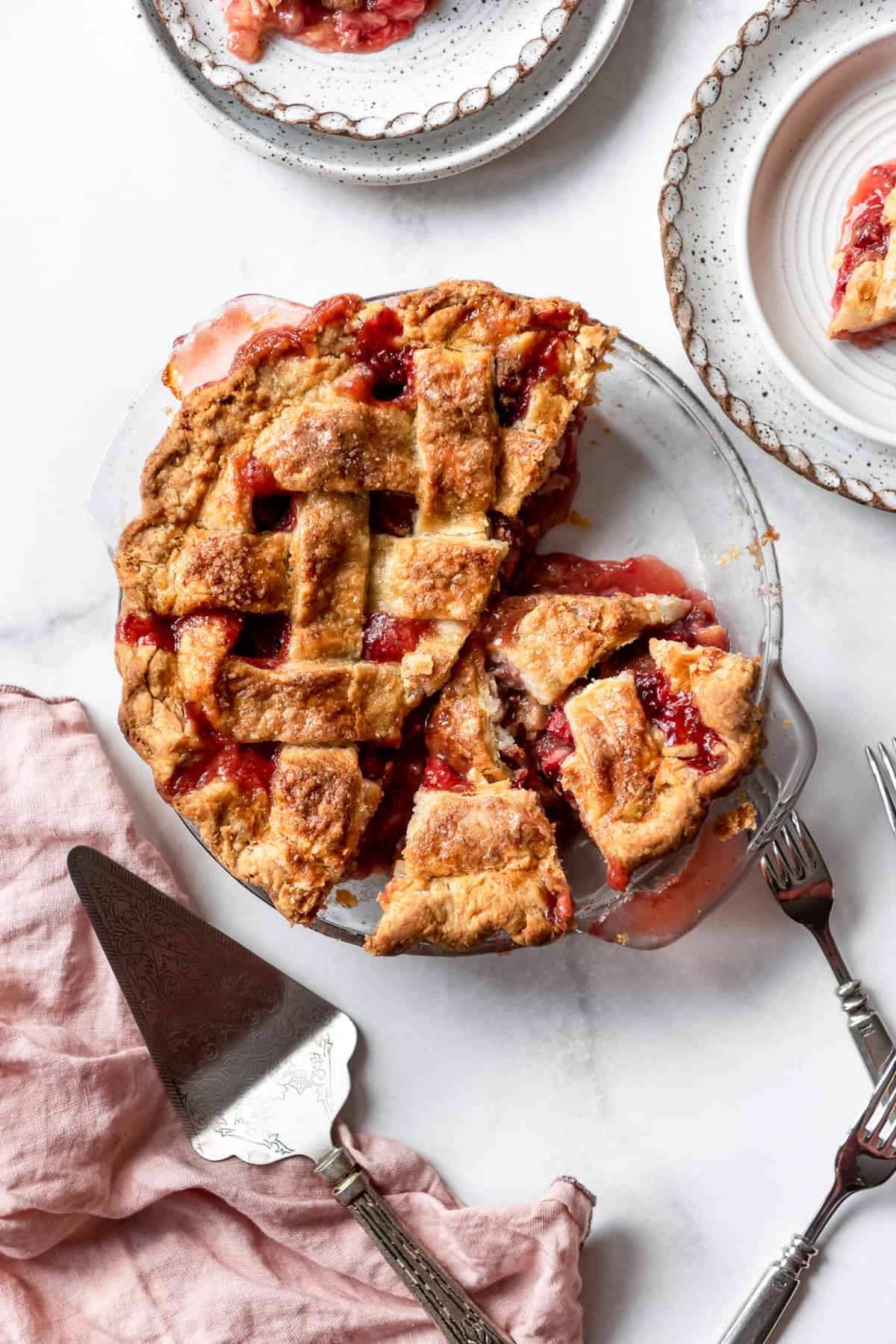 A strawberry rhubarb pie with slices removed and set on nearby plates.