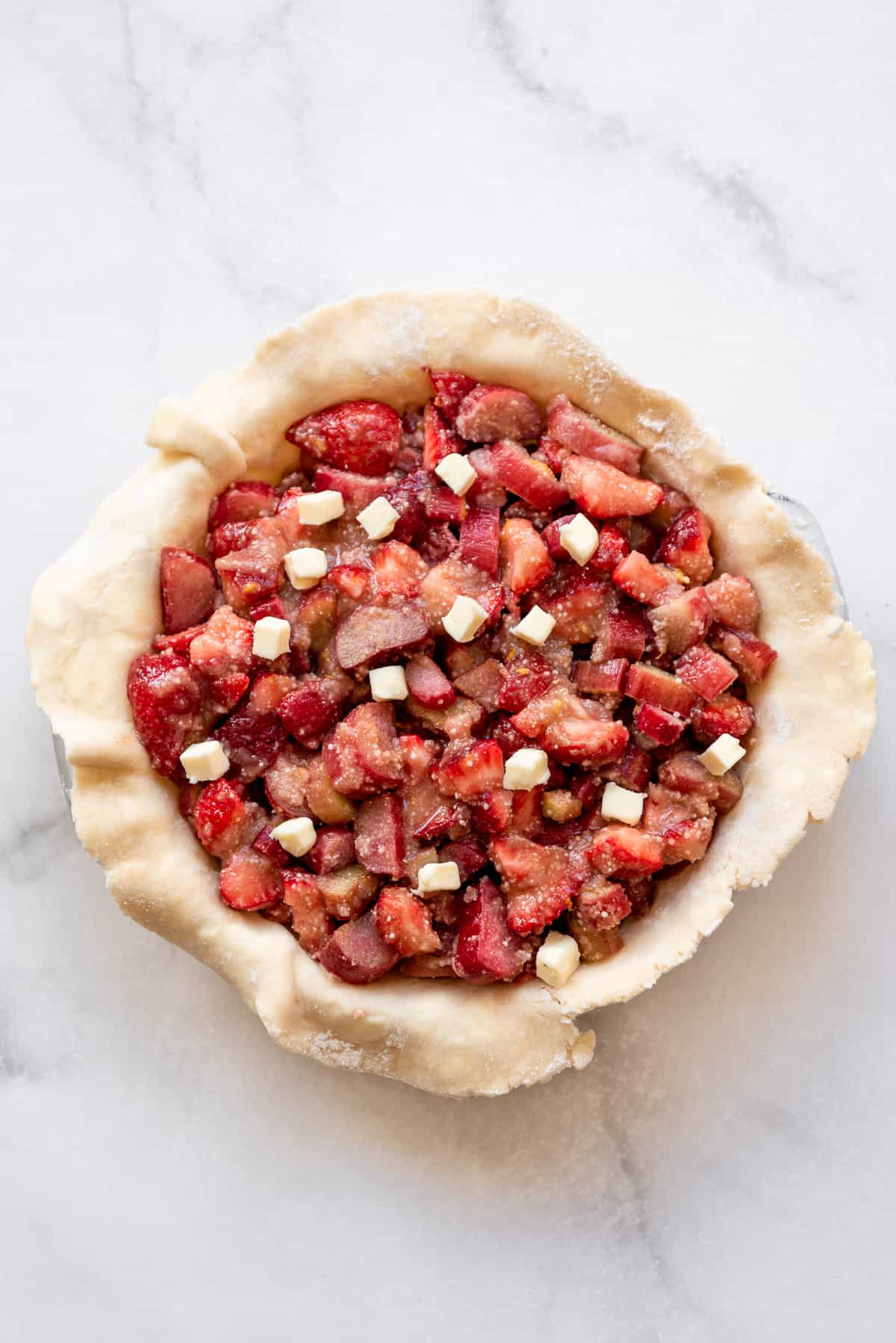 Strawberry rhubarb pie filling dotted with butter in a homemade pie crust.