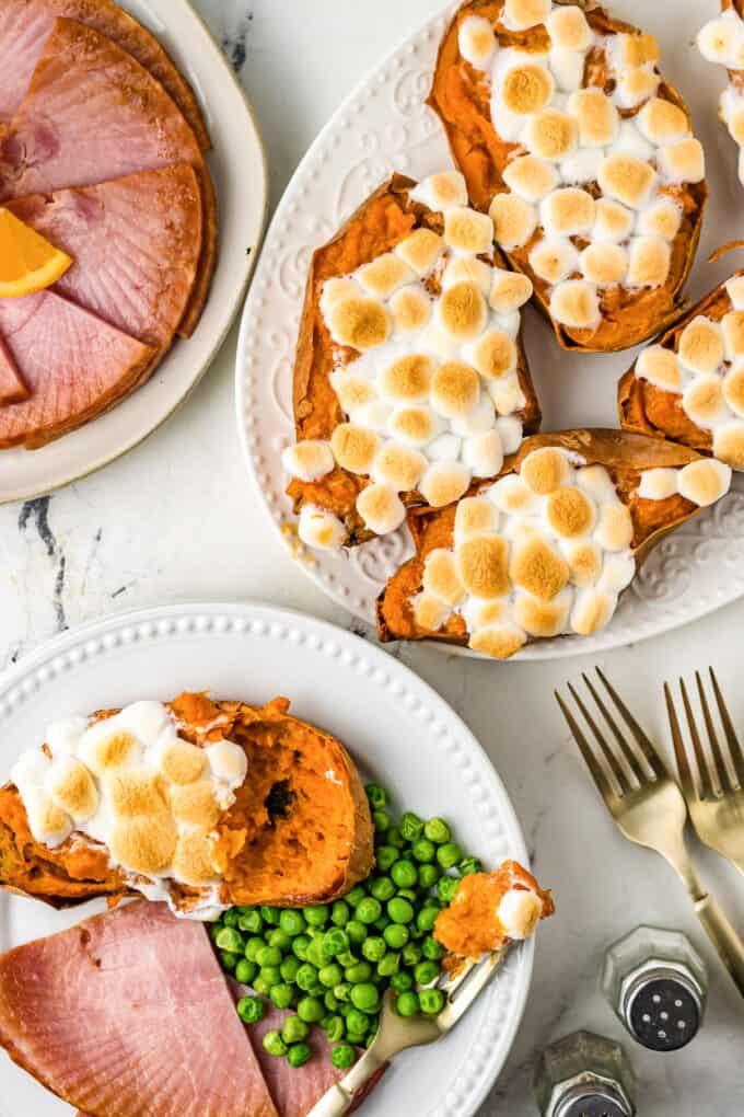 A plate with a twice baked sweet potato, ham, and peas, beside a platter of more sweet potatoes.