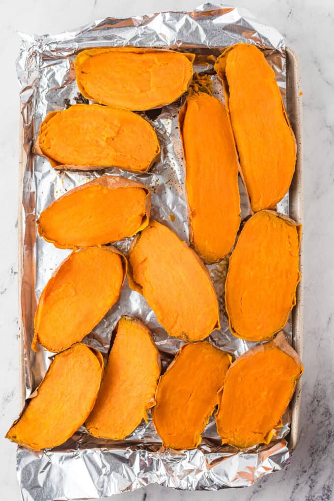 Baked sweet potatoes sliced in half on a baking sheet lined with foil.