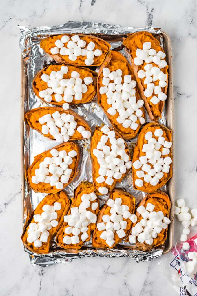 Marshmallows sprinkled on top of creamy mashed sweet potatoes in their skins.
