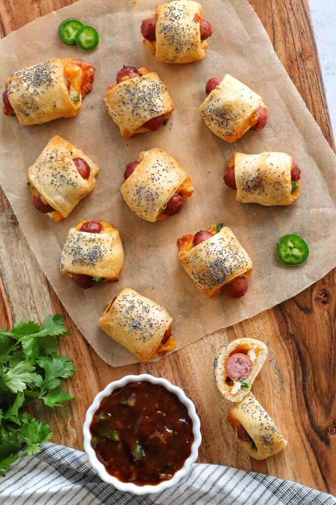 An overhead image of jalapeno popper pigs in a blanket with dipping sauce on parchment paper.