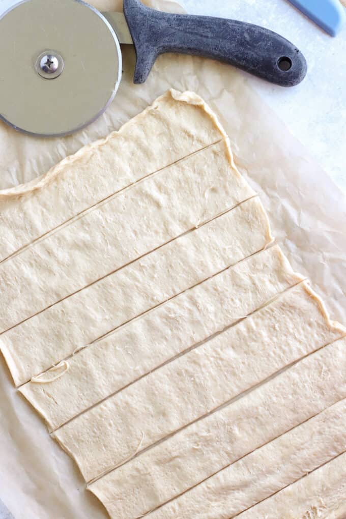 A sheet of crescent roll dough cut into strips.