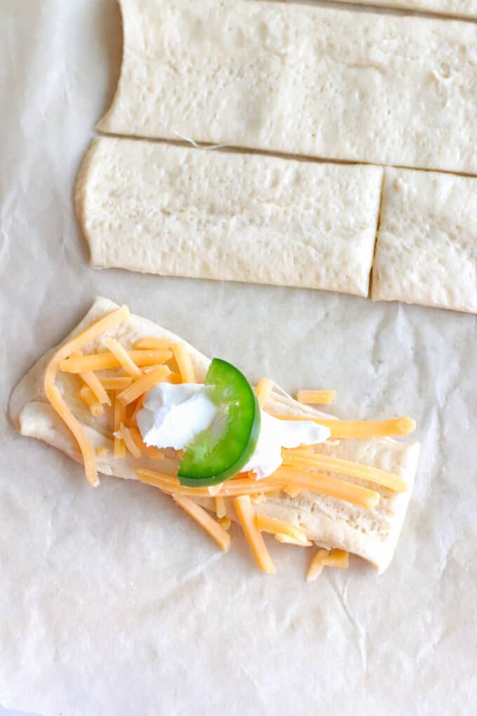 Arranging a slice of jalapeno on top of cream cheese and cheddar cheese on crescent roll dough.