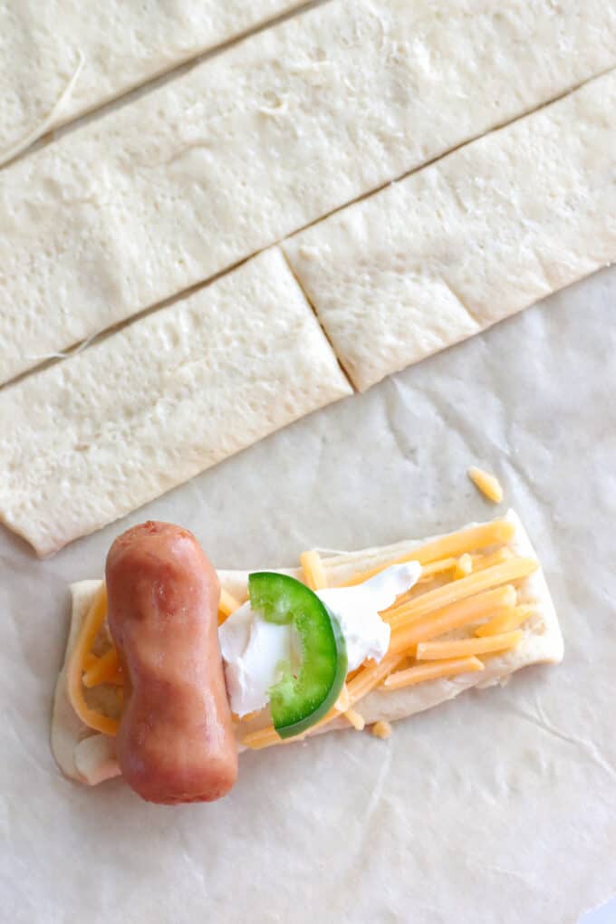 Wrapping cocktail weiners in crescent roll dough with cream cheese, cheddar cheese, and a slice of jalapeno.