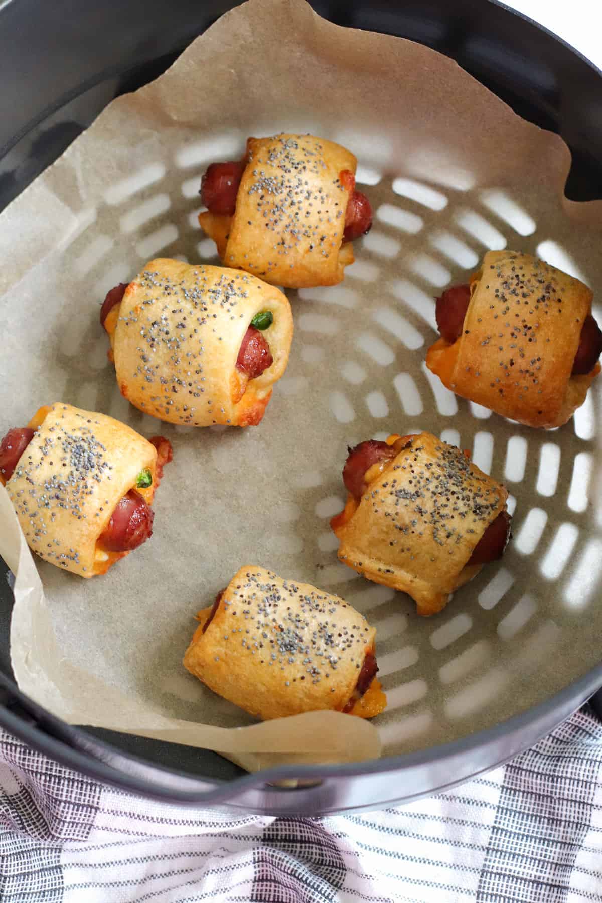 Pigs in a blanket in an air fryer basket lined with parchment paper.