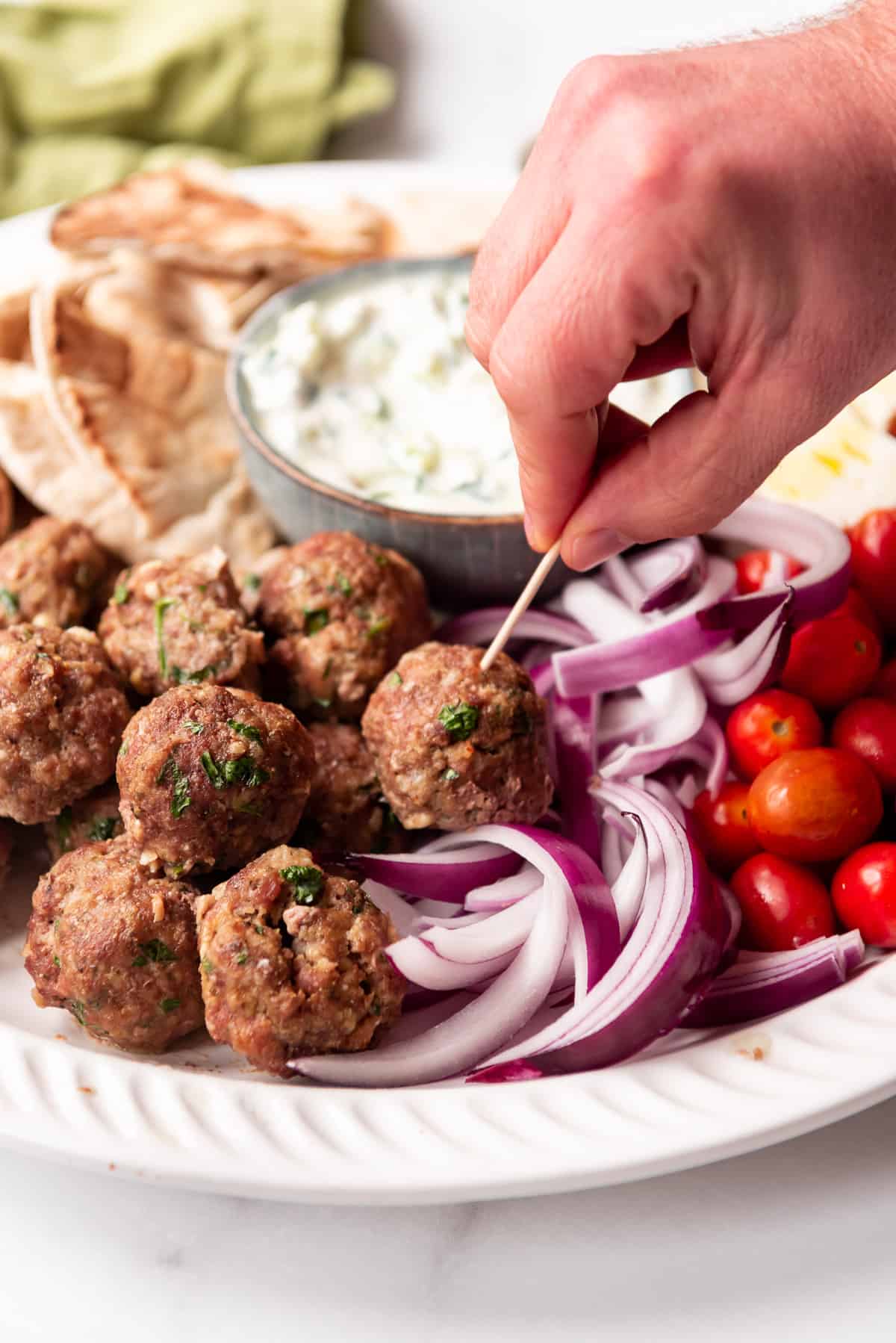 A hand picking up a meatball with a toothpick.