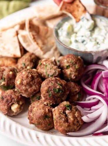 Baked Greek meatballs on a meze platter with tzatziki sauce, pita, and red onions.